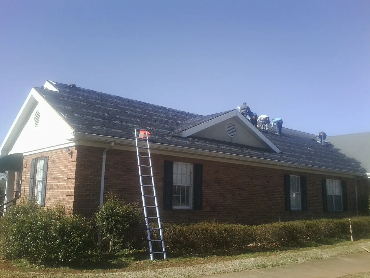 Crew tearing shingles off a brick ranch roof with a ladder set — Metal Roof Repair work by our crew in Tuckerton