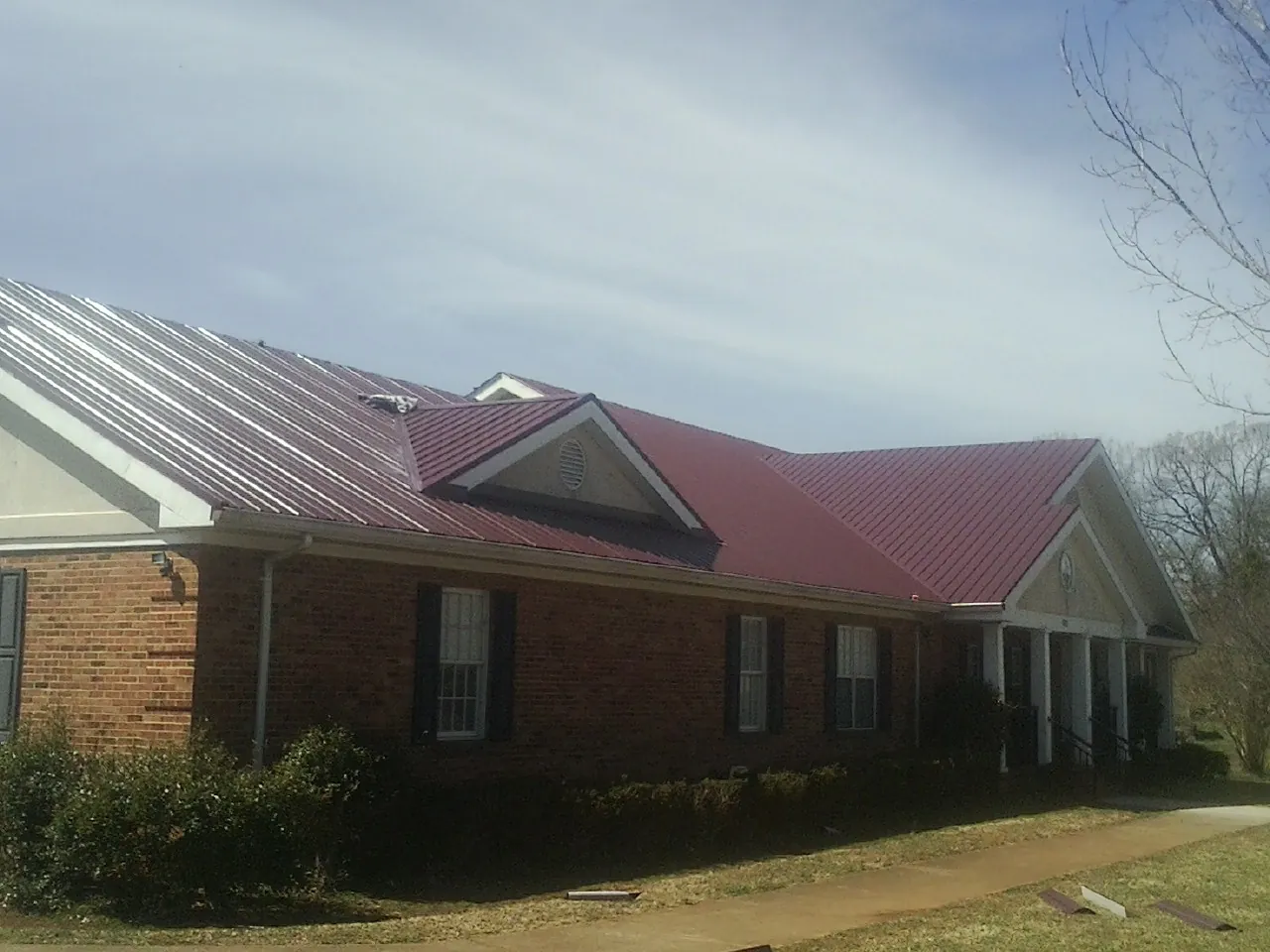 Red metal roof with gabled entries on a long brick building, from a Hail Damage Roof Repair job in Tuckerton