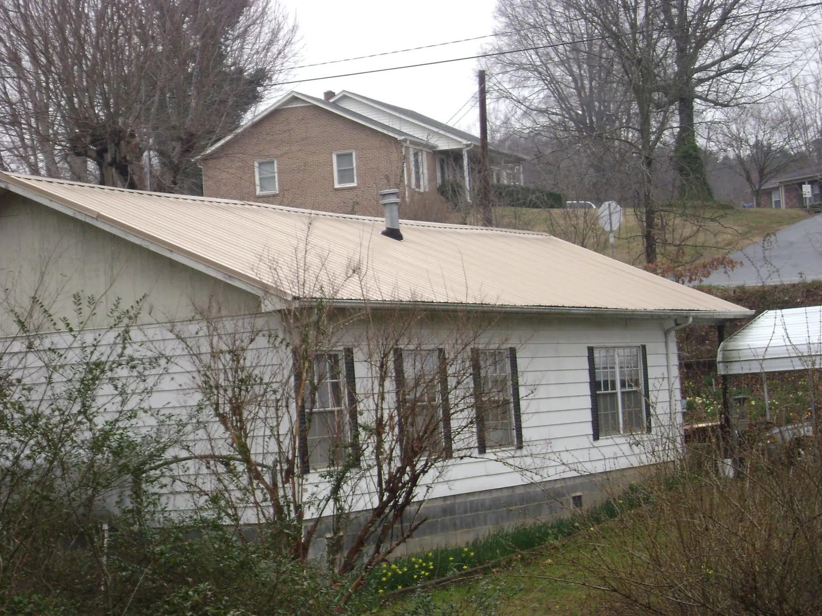 Tan metal roof on a white sided house set into a hillside — Commercial Roofing by Roofing Brothers in Tuckerton